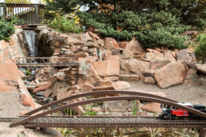 Model Train Running Outdoors Through a Bridge